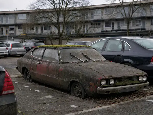 Verwaarloosde auto met lekke banden en mos op het dak op een parkeerterrein achter een flat